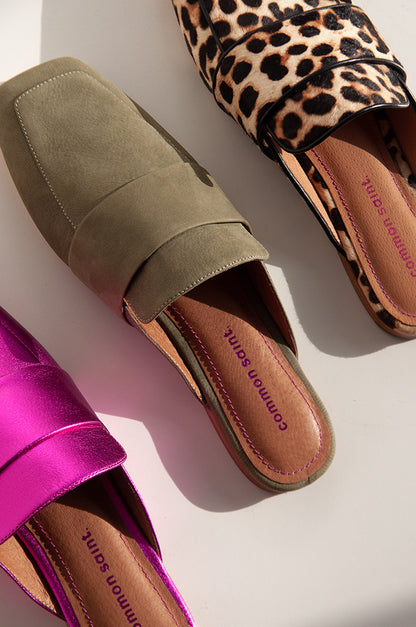 a lineup of 3 pairs of flat mules, photographed diagonally.  On the bottom left, is metallic pink, middle khaki leather mule, and top right is a leopard hair with black piping.  All mules have the brand common saint on footbed.